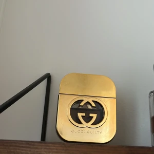 Gucci Guilty Eau de parfym (dam) - 50 ml. Endast provad. Elegant parfymflaska från Gucci Guilty i en lyxig guldfärg. Flaskan har en unik design med det ikoniska Gucci-emblemet i mitten. Perfekt för den som vill ha en sofistikerad doftupplevelse.