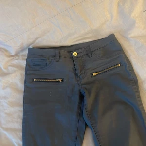 Svarta byxor med dragkedjor från Vila - Snygga svarta byxor från Vila med coola dragkedjor på framsidan. Byxorna har en stilren design med knapp och dragkedja i gylfen. Perfekta för en trendig look.