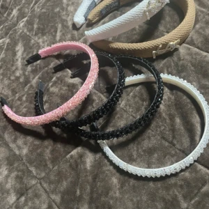 Flera diadem i olika färger och material - Säljer ett set med eleganta diadem i olika färger och material. Inkluderar ett beige och ett vitt diadem med pärldetaljer, samt rosa, svarta och vita diadem med glittriga detaljer. Perfekt för att ge en stilfull touch till din outfit.