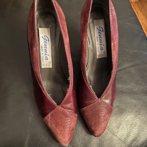 Vinröda pumps från Gennia - Snygga vinröda pumps från Gennia med spetsig tå och ett elegant mönster. Tillverkade i Spanien, dessa skor kombinerar stil och komfort perfekt. Perfekta för att ge en touch av elegans till din outfit.