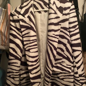 Zebramönstrad kavaj - Säljer en supercool zebramönstrad kavaj i svart och vit., med fickor Perfekt för att sticka ut på festen eller nyår! Den har en klassisk passform med långa ärmar och knappar framtill. Materialet känns lyxigt och är perfekt för både höst och vår. Ett måste för garderoben om du gillar djärva mönster!