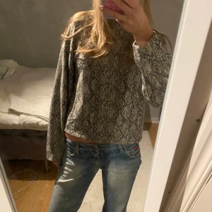 Orm-mönstrad tröja i brun o svart - Säljer en snygg och bekväm mönstrad tröja i grått och svart. Den har en loose passform och långa ärmar, perfekt för höst och vinter. Tröjan är i mycket bra skick och passar både till vardags och lite finare tillfällen. Perfekt att matcha med jeans eller kjol!