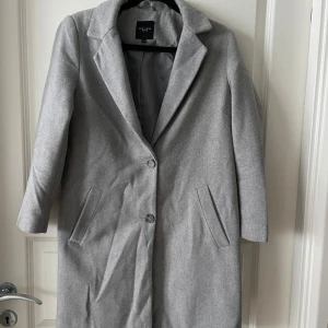 Grå kappa från New Look - Säljer en stilren grå kappa från New Look i storlek 8. Den har en klassisk design med knappar framtill och långa ärmar. Perfekt för höst och vår, och ger en elegant touch till vilken outfit som helst. Kappan är i mycket bra skick och redo för nya äventyr!