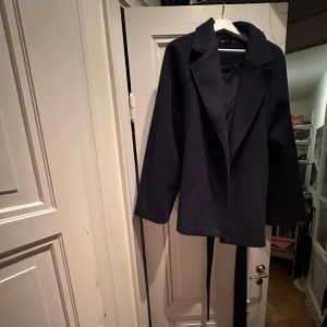 Mörkblå kappa  - Säljer en stilren mörkblå kappa i mycket bra skick. Inköpt för 6 månader sedan. Den har långa ärmar och ett matchande bälte för att ge en snygg siluett. Köpt i strl XL om man vill ha oversized/baggy look. Perfekt för höst och vår när du vill hålla dig varm och chic. Passar både till vardags och festliga tillfällen💙