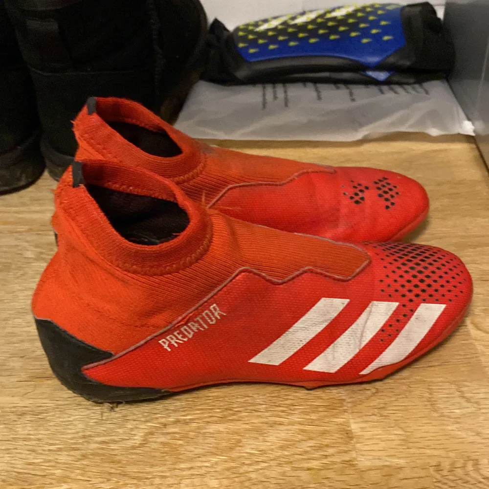 Säljer ett par röda Adidas Predator fotbollsskor i bra skick. De har en snygg design med vita detaljer och är perfekta för fotbollsträning. Skorna har en tight passform och är gjorda i syntetmaterial för bästa prestanda på planen.. Skor.