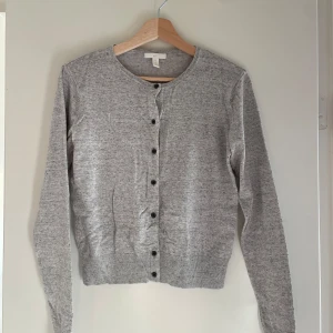 Grå kofta från Basics - Säljer en stilren grå kofta från Basics i storlek S. Den är i mycket bra skick och har en klassisk design med knappar framtill. Perfekt för både höst och vår, och funkar lika bra till vardags som till lite finare tillfällen. Supermjuk och bekväm att ha på sig!
