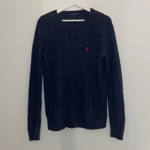 Mörkblå stickad tröja från Ralph Lauren - Säljer en snygg mörkblå stickad tröja från Ralph Lauren i storlek L. Tröjan har ett klassiskt kabelstickat mönster och den röda loggan på bröstet. Inte heller jätteanvänd så den är i gott skick.