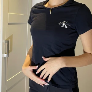 Svart t-shirt från Calvin Klein - Snygg svart t-shirt från Calvin Klein med deras  logga på bröstet. Perfekt för en casual look eller att klä upp med accessoarer. T-shirten har en normal passform och är kortärmad, vilket gör den idealisk för vardagen.