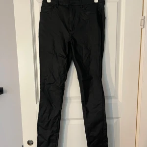Svarta byxor - Säljer ett par svarta skinnbyxor i bra skick. De har en klassisk stil med en rak passform och är perfekta för både vardag och fest. Byxorna har en dragkedja och knappar framtill. Passar till alla säsonger och är ett måste i garderoben!