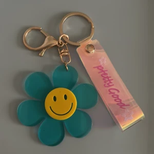Nyckelring med blomma och smiley - Supersöt nyckelring med en stor blomma i turkos och en glad gul smiley i mitten. 