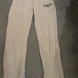 Beige mjukisbyxor från Lexington - Säljer ett par superbekväma beige mjukisbyxor från Lexington. Perfekta för en chill dag hemma eller en avslappnad promenad. Byxorna har en klassisk design med Lexington-loggan tryckt på sidan. De är i bra skick och gjorda av mjukt material som känns skönt mot huden.