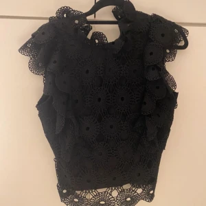Svart spetsblus - Säljer en elegant svart spetsblus med vackra detaljer. Blusen har volanger och är perfekt för festliga tillfällen.