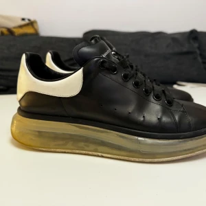 Svarta sneakers från Alexander McQueen - Säljer ett par svarta sneakers från Alexander McQueen i skinn med vit häl och genomskinlig sula. Skorna har snörning och är i bra skick. Perfekta för både vardag och fest!