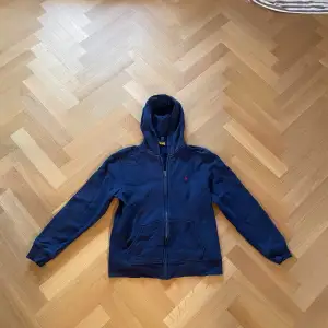 Säljer en snygg mörkblå hoodie från Polo Ralph Lauren i storlek L/G dvs 14-16. Den har en dragkedja och en klassisk röd logga på bröstet. Perfekt klassisk tjocktröja för alla tillfällen. Säljer den nu endast för 399 då nypris ligger på runt 1200 kronor! Skriv gärna i DM om ni har några frågor! Mvh Sthlm garderoben.