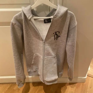 Grå zip hoodie från Softwear UF - Säljer en grå hoodie från Softwear UF i mycket bra skick. Den har en dragkedja framtill och en snygg logga på bröstet. Perfekt för både höst och vår, och den är supermjuk och bekväm. Passar till alla tillfällen!