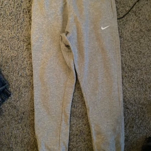 Grå mjukisbyxor från Nike - Säljer ett par grå mjukisbyxor från Nike i bra skick. De är superbekväma och perfekta för chill dagar eller träning. Byxorna har en normal passform och är gjorda av mjukt bomullsmaterial. Det klassiska Nike-loggan syns på benet. Perfekta för höst och vinter!