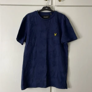 Mörkblå t-shirt från Lyle & Scott - Säljer en snygg mörkblå t-shirt från Lyle & Scott i bomull. Den är i storlek S. Mönstret är olika blad över hela tröjan. Säljs pågrund av liten användning.