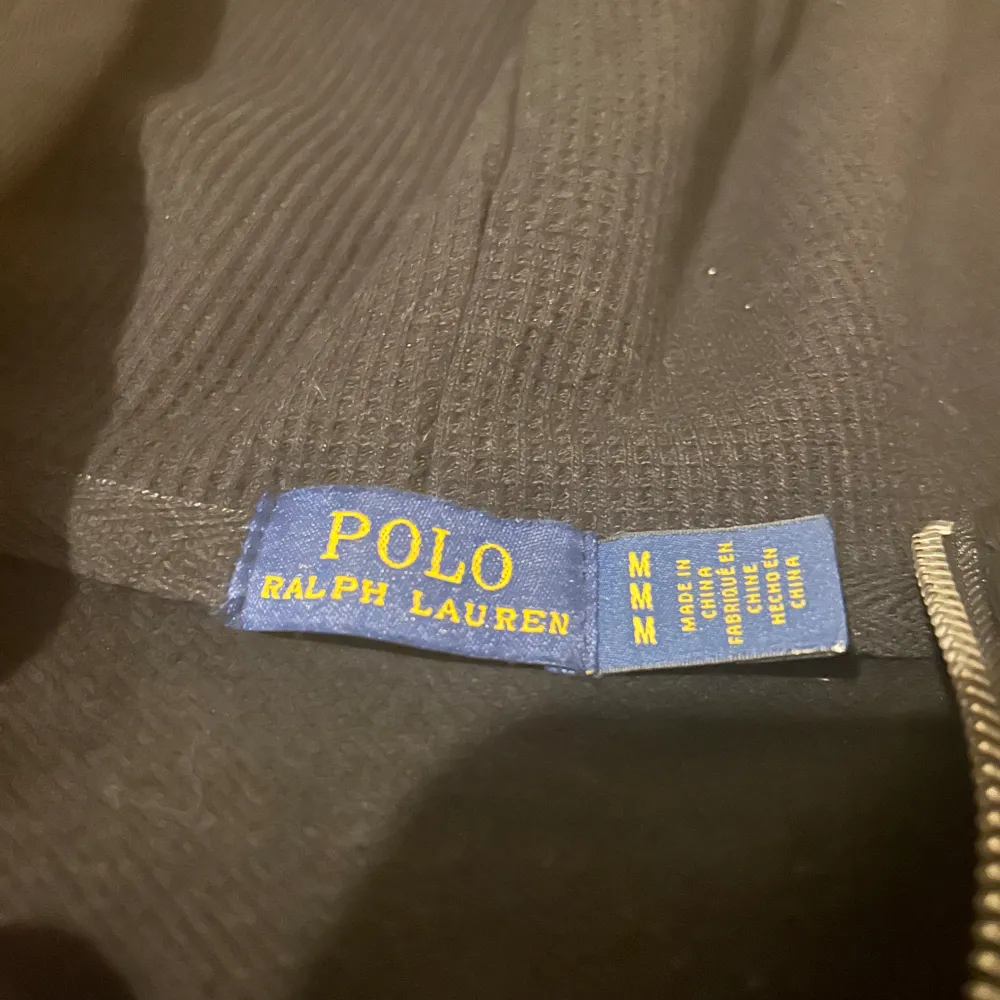 Säljer en snygg svart hoodie från Polo Ralph Lauren i storlek M. Den har en dragkedja framtill och en klassisk röd logga på bröstet. Perfekt för höst och vinter, både stilren och bekväm. Passar till alla tillfällen!. Tröjor & Koftor.