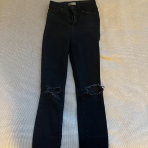 Svarta jeans med slitningar - Säljer ett par svarta jeans från Gina Tricot i storlek 34. De har en snygg slitning vid knäna som ger en cool look. Perfekta för både vardag och fest! 🖤