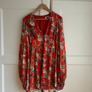 Röd blommig klänning från ADOORE - Säljer en superfin röd klänning från ADOORE i storlek 38. Den har en v-ringad design. Klänningen har långa ärmar och en dragkedja i ryggen. Perfekt för vår och sommar! 💘