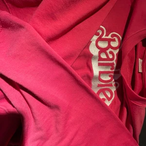 Rosa Barbie-tröja - Superfin rosa tröja med Barbie-logga i silver på bröstet. Perfekt för alla Barbie-fans som vill ha en färgglad och bekväm stil. Tröjan har en normal passform och är gjord i mjukt material för extra komfort. Ett måste för garderoben! 💖