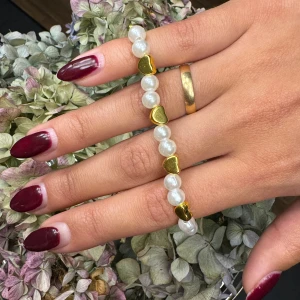 Pärlarmband med guldfärgade hjärtan - Snyggt armband med vita pärlor och guldfärgade hjärtan som heter ”Dahlia”. Perfekt för att ge en snygg touch till din outfit. Armbandet är elastiskt och passar till alla handleder. Perfekt för både vardag och fest!