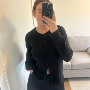 Svart kofta från GAP - Säljer en stilren svart kofta från GAP i mycket bra skick. Den har långa ärmar och knappar hela vägen fram. Perfekt för både vardag och festliga tillfällen. Passar bra till en kjol eller över en klänning för en elegant look.