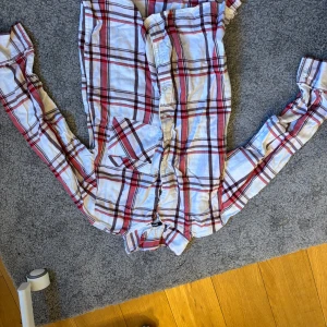 Rutig skjorta från Gina tricot  - Säljer en snygg rutig skjorta från Gini & Jony i vitt och rött med inslag av brunt. Skjortan har långa ärmar och knappar framtill. Perfekt för en avslappnad stil.