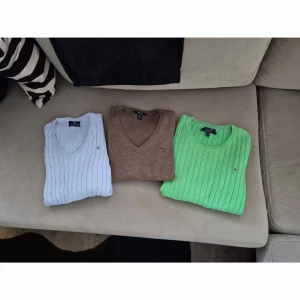 Trio av stickade tröjor från Gant - Säljer tre snygga stickade tröjor från Gant i olika färger: ljusblå, brun och grön. Alla tröjor har ett klassiskt kabelstickat mönster och v-ringad design. Perfekta för att hålla stilen året runt. Passar bra till både jeans och kjol!