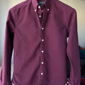 East West oxfordskjorta vinröd skjorta, storlek S - Vinröd oxfordskjorta från East West. Slim fit, storlek S. 100% bomull. Bra skick, något urtvättad. Button down. Jag säljer många skjortor i samma storlek, kolla gärna på mina övriga annonser för att skapa ett paket. Axelbredd: 43 cm Längd: 70 cm  Casual skjorta, smart, oxford.