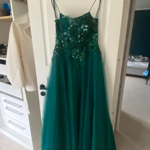 Superfin balklänning  - Grön balklänning med snörning i ryggen, ett litet släp, och som en korsett. Väldigt bekväm endast använd en gång sommaren 24, köptes för närmare 2000kr säljer den för 1700kr väldigt fint skick då den bara e använd en gång. Stl 38. Har ni frågor är de bara att ställa. 