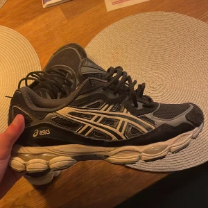 Asics nyc gel - Säljer ett par svarta Asics sneakers med vita detaljer och snörning. Skorna har en robust sula och är perfekta för träning eller vardagsbruk. De har en sportig design med Asics logotyp på sidan. Låda och kvitto ingår