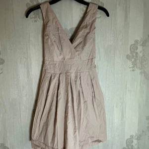 Rosa klänning med knytband - Säljer en söt rosa klänning med v-ringning och knytband i midjan. Klänningen har breda axelband och en smockad rygg för extra komfort. Perfekt för sommarens alla tillfällen! Storlek S/M