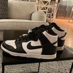 Svartvita Nike Dunk sneakers - Snygga svartvita Nike Dunk sneakers med klassisk design. Skorna har en hög siluett med snörning och den ikoniska Nike-loggan på sidan. Perfekta för en stilren look. Pris går att diskuteras
