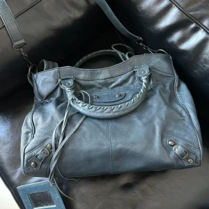 Blå axelväska med dragkedja - Snygg blå axelväska i skinn med flätade handtag och justerbar axelrem. Väskan har flera nitar och en praktisk dragkedja på framsidan. Perfekt för att bära med sig det viktigaste med stil. Size 36x26cm