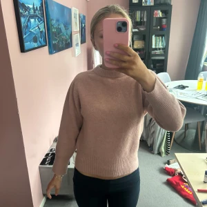 Rosa stickad tröja med öppen rygg - Säljer en mysig rosa stickad tröja med en unik öppen ryggdetalj. Tröjan har långa ärmar och en rund halsringning. Perfekt för en stilren och bekväm look. Passar bra till både jeans och kjol.