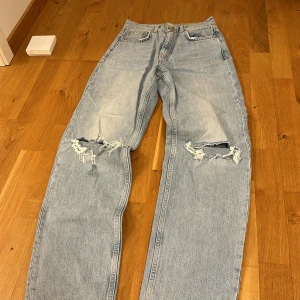 Ljusa jeans med slitningar från Gina tricot  - Säljer ett par ljusa jeans från Gina tricot med coola slitningar på knäna. De har en klassisk femficksdesign och knappgylf. Perfekta för en avslappnad stil.