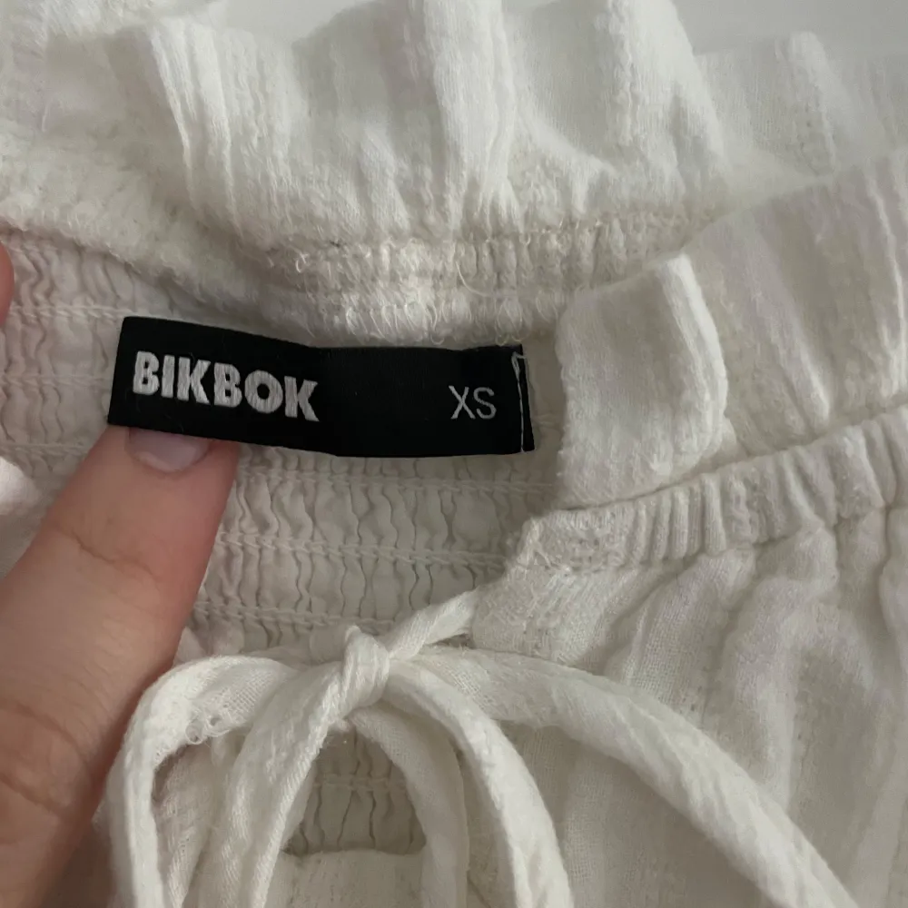 En aldrig använd söt vit klänning från BikBok i storlek XS. Klänningen har en offshoulder-design med volangdetaljer och knyt framtill. Perfekt för sommaren, skolavslutning eller student!. Mekot.