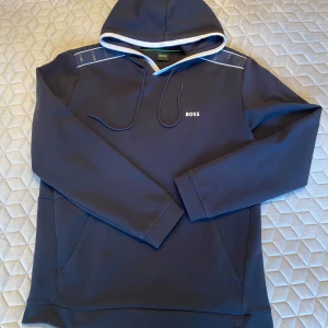 Hugo Boss hoodie - Snygg mörkblå hoodie från BOSS med vit kant på huvan och diskret logga på bröstet. Perfekt för en stilren och avslappnad look. Inget lurv på insidan, lite svalare än standard hoodie