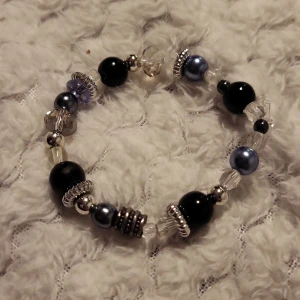Armband med pärlor i olika färger - Charmigt armband med en mix av pärlor i svart, silver och blå nyanser. Armbandet har detaljerade silverfärgade mellanpärlor som ger en elegant touch. Perfekt för att lägga till lite glans till din outfit.