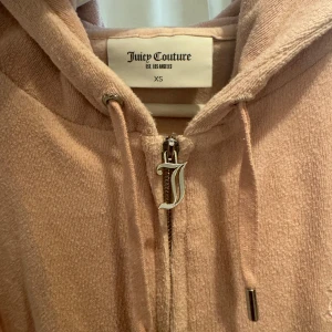 Kofta Juicy Couture - Säljer en snygg beige/rosa hoodie från Juicy Couture i storlek XS. Detta är inte velour kollektionen utan har ett frotté material och har ett broderat "J" på bröstet , digitalt kvitto finns om så önskas!💕