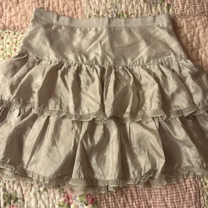 Beige volangkjol från Custommade - Säljer en supersöt beige kjol från Custommade med flera lager av volanger och en dragkedja bak. Den är ganska kort och är tillverkad i ett lätt/tunnt material så toppen för sommaren! Den passar mig perfekt som en storlek 38 ungefär. Man kan ha den både som low-waist och high-waist!