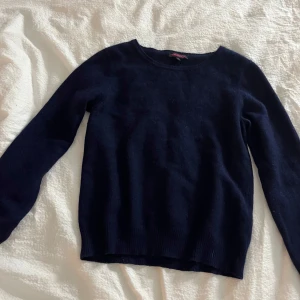 Mörkblå tröja från Indiska - Säljer en stilren mörkblå tröja från Indiska. Tröjan har en klassisk rund halsringning och långa ärmar, perfekt för kyligare dagar. Den är mjuk och bekväm, idealisk för både vardag och avslappnade tillfällen.