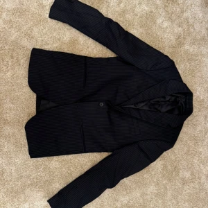 Svart randig kavaj från Riley - Missa inte chansen till denna populära kavajmodell. Svart, kritstrecksrandig kavaj från Riley (Brothers) i slim fit modell. Klassisk design med knäppning framtill och fickor. Använd 2 gånger. I mycket bra skick och har en väldigt skön passform, som är normal.  Varumärke Storlek kavaj: 46 Ord. Pris: 699 Färg: svart med vita ränder  Din stil: spara inlägget så du inte missar denna kappa Inte din stil: Kolla min profil. Du kommer hitta något för alla kön och åldrar.