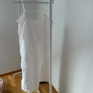 Vit ärmlös klänning - Säljer en stilren vit ärmlös klänning med smala axelband. Perfekt för varma sommardagar. Klänningen har en enkel och luftig design som ger en avslappnad känsla.