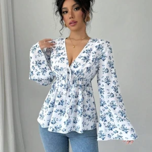 Vit blommig blus med knytning - Säljer en söt vit blus med blått blommönster och knytning framtill. Blusen har långa ärmar och en v-ringad design som ger en romantisk touch. Aldrig använd!!!! Storlek M. 