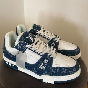 Blå och vita sneakers från Louis Vuitton - Snygga sneakers i blått och vitt från Louis Vuitton med monogrammönster. Skorna har snörning och en robust sula. Perfekta för att ge din outfit en lyxig touch.