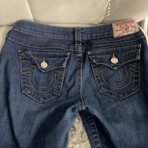  True Religion - Snygga blå jeans från True Religion med klassisk femficksdesign och kontrastsömmar. Byxorna har en bootcut-stil och är tillverkade i en bomullsblandning för extra komfort. Super bra skick mrn har bara gjort hål gör att få genom sko snöre, men inget som syns.