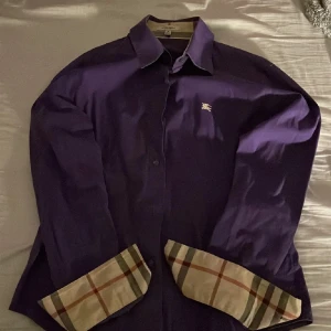 Lila skjorta från Burberry - Säljer en stilren lila skjorta från Burberry i storlek XXS. Skjortan är i mycket bra skick och är självklart äkta. Nypris ligger på runt 4000 och mitt pris är 499. Kan gå ner lite i pris vid snabb affär. Hör av er vid frågor eller funderingar!