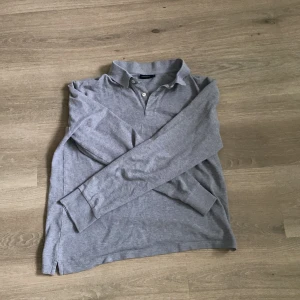 Långärmad pikétröja från J.Lindeberg - Säljer en stilren grå pikétröja från J.Lindeberg. Tröjan har långa ärmar och en klassisk krage med knappar. Perfekt för en avslappnad men ändå snygg look. Passar bra till både jeans och chinos. Storlek M.